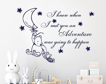 May include: A Winnie the Pooh inspired wall decal featuring a bear holding a crescent moon balloon. The decal includes the quote "I knew when I met you an adventure was going to happen." and stars.