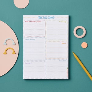 May include: A white shopping list notepad with a colorful design. The notepad is divided into sections for different categories of groceries, including meat and fish, fruit and vegetables, chilled and frozen, bakery, household, and cupboard. The notepad has the words "THE BIG SHOP" at the top.