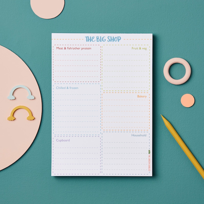 May include: A white notepad with a colorful grocery list titled "The Big Shop". The list is divided into six sections: Meat & fish/other protein, Fruit & veg, Chilled & frozen, Bakery, Household, and Cupboard. Each section has lines for writing.