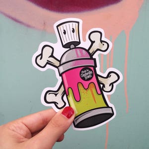 Könnte beinhalten: Rosa und grüne Sprühdose mit Totenkopf- und Knochen-Design. Die Dose trägt den Text "Made by Cinderella Bones".