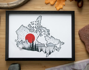 May include: A black framed print of a stylized map of Canada with a red sun setting over a mountain range. The print is on a wooden surface with a Canadian ten dollar bill, a pen, and various natural elements.