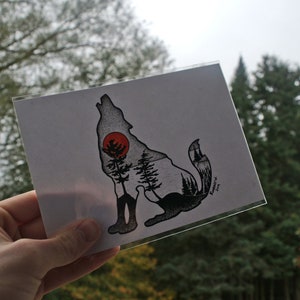 May include: A black and white illustration of a wolf howling at the moon. The wolf is silhouetted against a forest scene with a red sun in the background. The print is 5x7 inches.