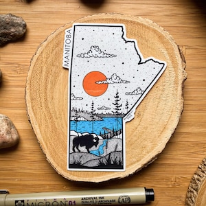 Op de afbeelding: Een zwart-witte illustratie van de Canadese provincie Manitoba. De illustratie toont een zonsondergang, een meer, bomen en een bizon. De tekst "MANITOBA" staat verticaal aan de linkerkant van de illustratie.