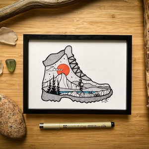 Puede incluir: Una ilustración en blanco y negro de una bota de senderismo con una escena de montaña en su interior. La bota está dibujada en un estilo punteado y presenta un sol rojo, un lago azul y una pequeña figura haciendo senderismo en las montañas. La ilustración está enmarcada en un marco negro.