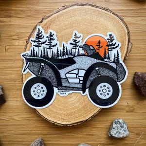 Könnte beinhalten: Schwarz-weiß-Illustration eines ATVs, das durch einen Wald fährt, mit einem Sonnenuntergang im Hintergrund. Das ATV hat ein schwarz-weißes, punktiertes Design und der Text "Foxrad W. 2014" ist an der Seite sichtbar.
