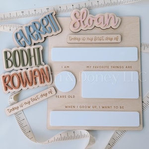 May include: A wooden milestone board with the names "Everett", "Bodhi", "Rowan", and "Sloan" in various colors. The board includes spaces for "I am", "My favorite things are", and "When I grow up, I want to be". The text "today is my first day of" and "today is my last day of" are also present.