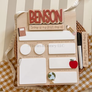 May include: A wooden school milestone board featuring the name BENSON in red letters, with white dry-erase sections for age, height, career goals, favorite things, teacher, and date. Includes a black marker, a pencil icon, and a globe icon.