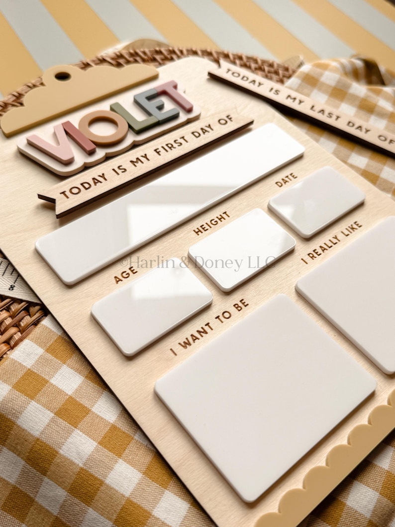 May include: A wooden milestone board featuring the name VIOLET in raised, multi-colored letters. The board includes text sections for Today Is My First Day Of, Today Is My Last Day Of, Date, Height, Age, I Really Like, and I Want To Be.