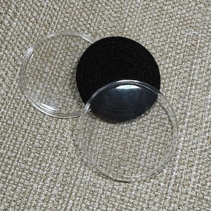 Puede incluir: Dos discos redondos de plástico transparente y una almohadilla circular de fieltro negro. La almohadilla de fieltro está formada por círculos concéntricos.