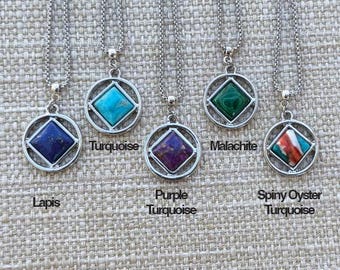 Puede incluir: Cinco collares de plata con colgantes de piedras preciosas de diferentes colores. Los colgantes son de forma cuadrada y están engastados en un marco redondo de plata. Las piedras preciosas son turquesa, lapislázuli, turquesa púrpura, malaquita y turquesa de ostra espinosa.
