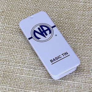 Puede incluir: Lata de metal blanca con un logotipo NA azul y el texto "BASIC TIN".