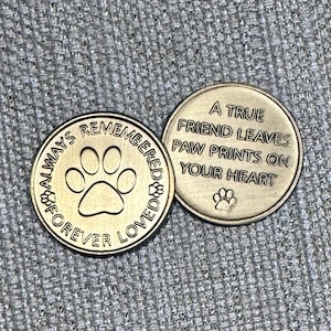 May include: Two gold-colored metal tokens with paw print designs. One token reads "Always Remembered Forever Loved" with a paw print in the center. The other token reads "A True Friend Leaves Paw Prints On Your Heart" with a smaller paw print at the bottom.