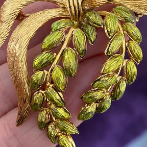 May include: A gold tone brooch with a green enamel bow and leaves. The bow has a rhinestone in the center.