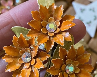 May include: A vintage brooch featuring three orange enamel flowers with gold-tone leaves and sparkling rhinestone centres.