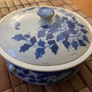 May include: A white ceramic bowl with a blue and white floral design. The bowl has a lid with a knob on top. The bowl is decorated with a floral pattern in shades of blue.