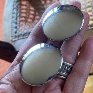 May include: A pair of large, round, silver-toned earrings. The earrings are smooth and have a high polish.