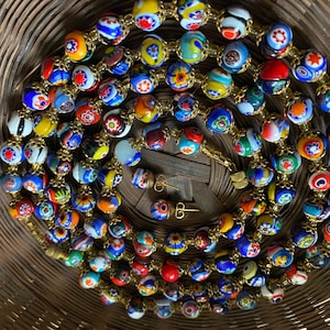May include: A colorful necklace and matching earrings featuring millefiori glass beads. The beads are round, with a variety of floral and abstract patterns in red, blue, yellow, and white. The necklace and earrings have gold-colored metal accents.