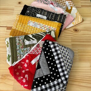 Peut inclure: Un ensemble de 8 pochettes zippées matelassées colorées avec différents motifs. Chaque pochette porte une étiquette indiquant "L'atelier de Claire" et "Made for Handmade".