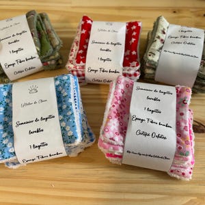 Peut inclure: Cinq piles de lingettes réutilisables à motifs floraux, dont bleu, rose et vert. Chaque pile est enveloppée d'une bande de papier avec du texte en français. Les lingettes sont en fibre de bambou.