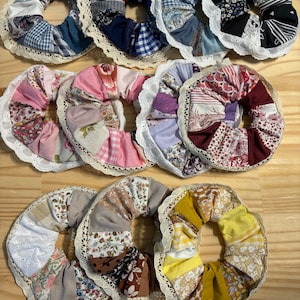 Peut inclure: Une collection de dix chouchous en tissu faits à la main avec une variété de motifs floraux et géométriques. Chaque chouchou est orné d'une bordure en dentelle blanche.