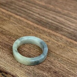 Op de afbeelding: Een eenvoudige, witte en grijze ring van jade. De ring is glad en gepolijst, met een subtiel marmerpatroon.