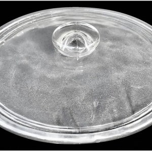 Könnte beinhalten: Ovaler Deckel aus klarem Glas mit einem kleinen, abgerundeten Griff. Der Deckel hat einen leicht erhöhten Rand und ist für einen Topf oder eine Pfanne konzipiert. Das Glas ist transparent, wodurch der Inhalt sichtbar ist. Für die Küche.