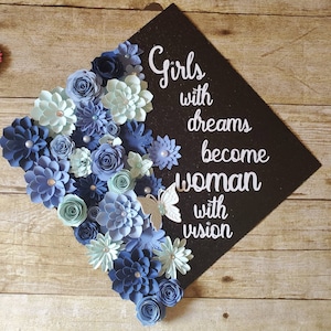 Op de afbeelding: Een afstudeerhoed versierd met blauwe en lichtblauwe papieren bloemen en een witte vlinder. Op de hoed staat de tekst "Girls with dreams become woman with vision".