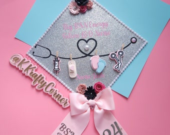 May include: A silver glitter graduation cap decorated with a stethoscope, heart, and medical-themed charms. The cap has text that reads "Big B&N Energy, Future R.N. Nurse." A pink ribbon with "BSN, RN" and the number "24" is attached.
