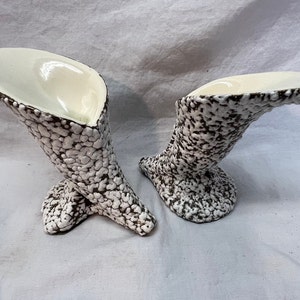 May include: Two white ceramic vases with a brown speckled glaze. The vases are shaped like a trumpet or horn and have a wide opening at the top.
