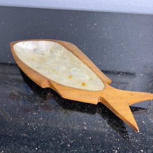 May include: A wooden fish-shaped dish with a white mother-of-pearl inlay. The dish is made of wood and has a natural finish.