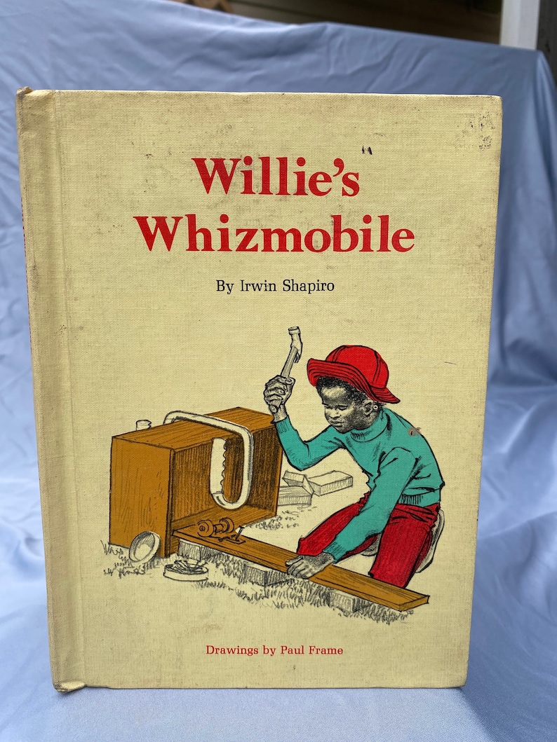 Puede incluir: Una portada de libro infantil vintage con el t&iacute;tulo "Willie's Whizmobile" en letras rojas. La portada presenta una ilustraci&oacute;n de un ni&ntilde;o peque&ntilde;o con un sombrero rojo usando un martillo para construir un coche de madera.