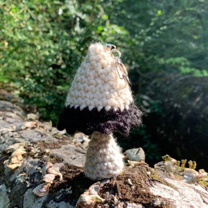 May include: A crocheted mushroom keyring with a white top and black bottom. The keyring is attached to a silver key ring.