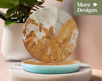 May include: A round marble coaster with a brown and white pattern rests on a marble base with a light blue edge. The image also features a potted plant and the text "More Designs".