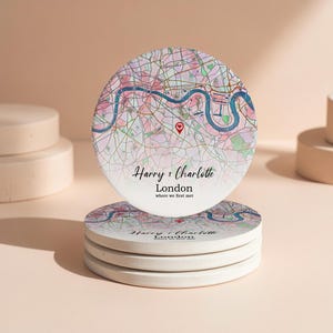 May include: Four round coasters stacked, each featuring a map of London in pink, blue, and beige. A red heart marks a location. Text on the top coaster reads "Harry & Charlotte, London where we first met".