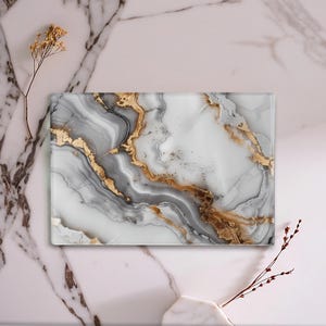 Könnte beinhalten: Rechteckiges dekoratives Glas-Schneidebrett mit Marmordesign. Das Design zeigt weiße, graue und goldene Maserungen. Das Schneidebrett wird auf einer Marmoroberfläche mit getrockneten floralen Akzenten präsentiert.