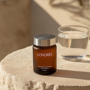 May include: A brown supplement bottle with a silver lid and the word "LONDRES" printed on the front. The bottle is next to a glass of water. The text "ADVANCED MULTIVITAMIN" and "60 TABLETS" are also visible on the bottle.
