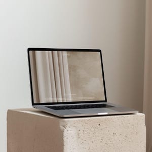 Pode incluir: Um laptop prateado exibindo um site com o texto "ONDRES" em uma tela bege clara. O laptop está colocado em um bloco de pedra clara e texturizada. O fundo é de cor branco sujo neutro.