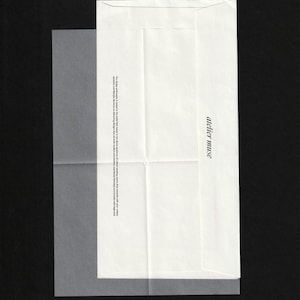 Könnte beinhalten: Ein weißer Papierumschlag mit dem Text "atelier muse" auf der Vorderseite. Ein durchscheinendes Blatt Papier ist links teilweise sichtbar. Der Umschlag hat ein gefaltetes Design und ist vor einem schwarzen Hintergrund platziert.