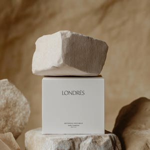 Może przedstawiać: Białe pudełko z napisem "LONDRÉS" i "BOTANICAL FACE BALM". Pudełko stoi na jasnobrązowej skale.