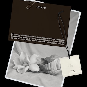 May include: A dark brown rectangular card with the text LE CACHET and a paragraph about mockup philosophy, attached by a black string to a small white square tag with a logo. Below, a black and white photograph shows a flower and a seashell.