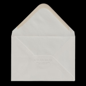 May include: An open, off-white envelope with a light brown interior. The envelope has a triangular flap and the text "ATELIER MUSE" is embossed on the front, along with the phrases "ETHICALLY MADE IN FRANCE" and "ATELIEMUSE.COM".