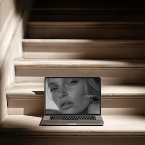 May include: A laptop displaying a black and white image of a woman's face with the word "LONDRES" in the lower right corner. The laptop is placed on a set of off-white stairs.