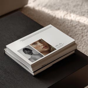 May include: A stack of books on a dark wood table. The top book features two images: a black and white photo of a woman's updo and a color portrait of a woman. The text "Atelier Muse" is visible on the cover.