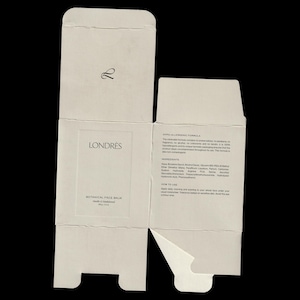 以下が含まれることがあります： Londrès Botanical Face Balmの、広げられたオフホワイトの段ボール箱。箱にはLondrèsのロゴ、製品名、成分リストが記載されています。箱は開いており、内部と製品情報が表示されています。