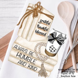 May include: A white kitchen towel featuring a graphic illustration of a stack of cream-colored books tied with twine, a coffee cup with a black and white buffalo check bow and heart, and a string of wooden beads with a tassel and printed text.