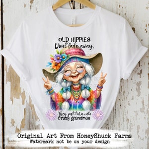 May include: A white t-shirt featuring a colourful illustration of a smiling woman with long white hair wearing a tie-dye shirt, a flower crown, and a peace sign necklace. The text "Old Hippies Don't Fade Away, They Just Turn Into Crazy Grandmas" is printed on the shirt.