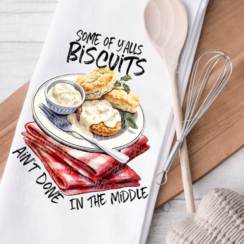 Op de afbeelding: Witte keukendoek met een rood-wit geblokte servet, een bord met biscuits en jus, en de tekst "Some of Y'alls Biscuits Ain't Done in the Middle".