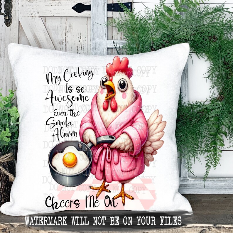Pu&ograve; includere: Un cuscino bianco con un motivo a quadri rosa e bianco. Un pollo dei cartoni animati che indossa una vestaglia rosa tiene una padella con un uovo fritto. Il testo sul cuscino recita "My Cooking Is So Awesome Even The Smoke Alarm Cheers Me On".