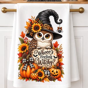 May include: A white kitchen towel featuring a brown owl wearing a black witch hat, surrounded by sunflowers, autumn leaves, and pumpkins. A wooden sign in the center displays the text Whooo's Feeling Witchy? with small bat silhouettes.