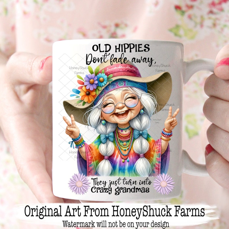 May include: White ceramic mug featuring a colourful illustration of a smiling woman with long white hair wearing a tie-dye shirt, a flower crown, and a peace sign. The text reads "Old Hippies Don't Fade Away, They Just Turn Into Crazy Grandmas".